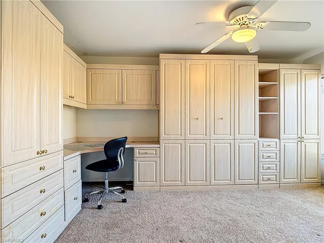Office area with built in study area, ceiling fan, and light carpet