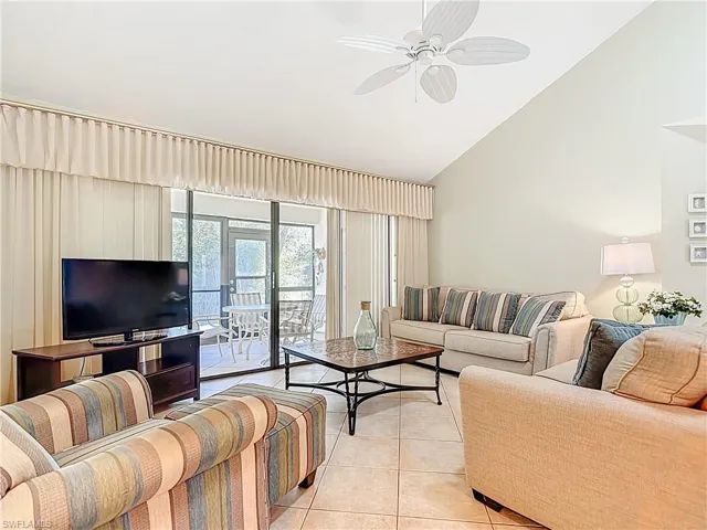 Living room with vaulted ceiling, light tile patterned flooring, and ceiling fan
