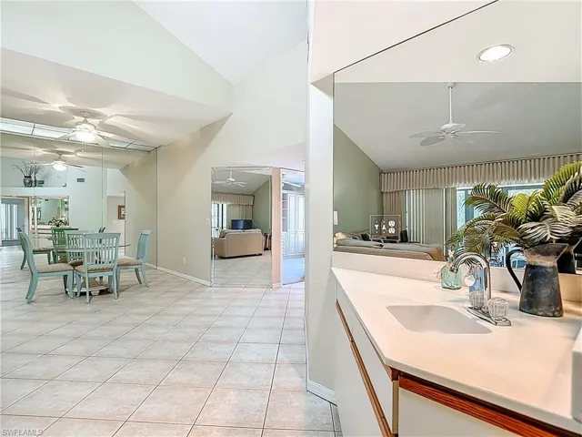 Kitchen featuring ceiling fan, vaulted ceiling, light tile patterned floors, white cabinets, and light stone counters