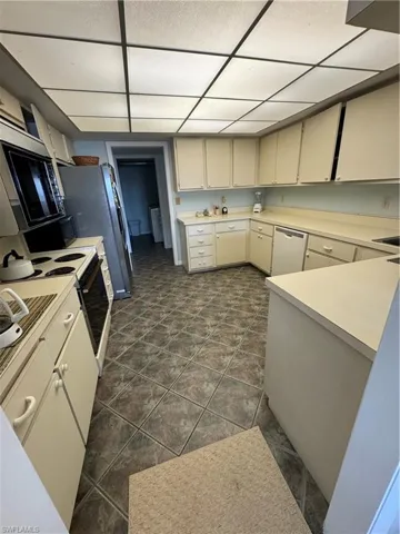 Kitchen with dishwashing machine, dark tile flooring, a paneled ceiling, and range