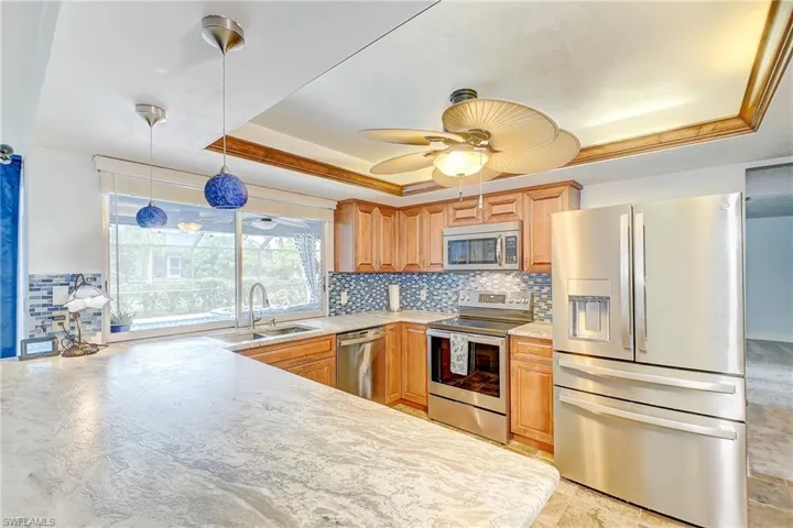 Kitchen with stainless steel appliances, hanging light fixtures, a tray ceiling, and sink