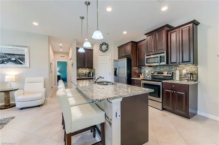 Kitchen featuring dark brown cabinetry, tasteful backsplash, appliances with stainless steel finishes, light stone countertops, and a kitchen breakfast bar