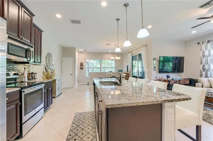 Kitchen featuring appliances with stainless steel finishes, dark brown cabinetry, light stone counters, a kitchen breakfast bar, and light tile patterned flooring