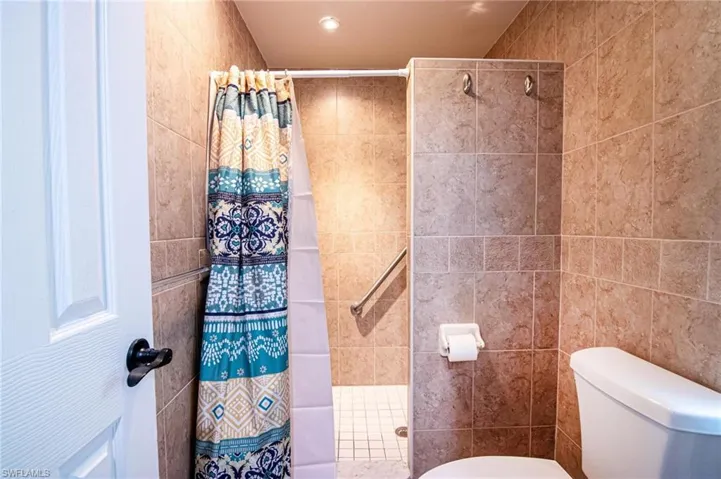 Bathroom featuring tile walls, toilet, and a shower with shower curtain