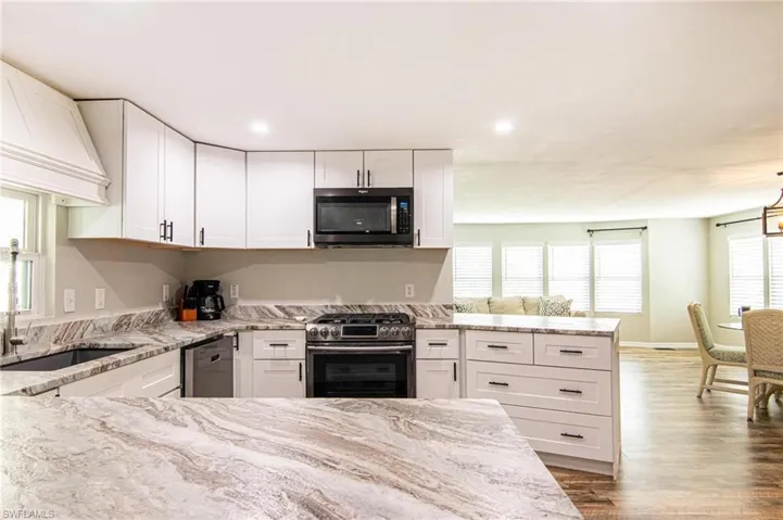 Kitchen featuring sink, white cabinetry, wood-type flooring, appliances with stainless steel finishes, and light stone countertops