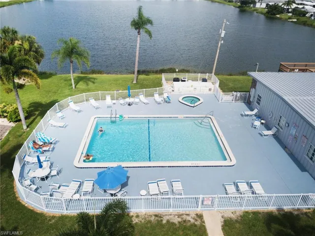 View of swimming pool featuring a hot tub, a water view, a lawn, and a patio area