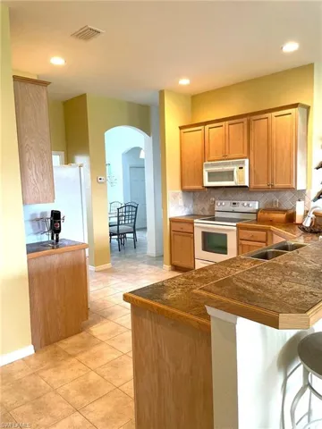 Kitchen with white appliances, backsplash, kitchen peninsula, a breakfast bar area, and light tile patterned flooring