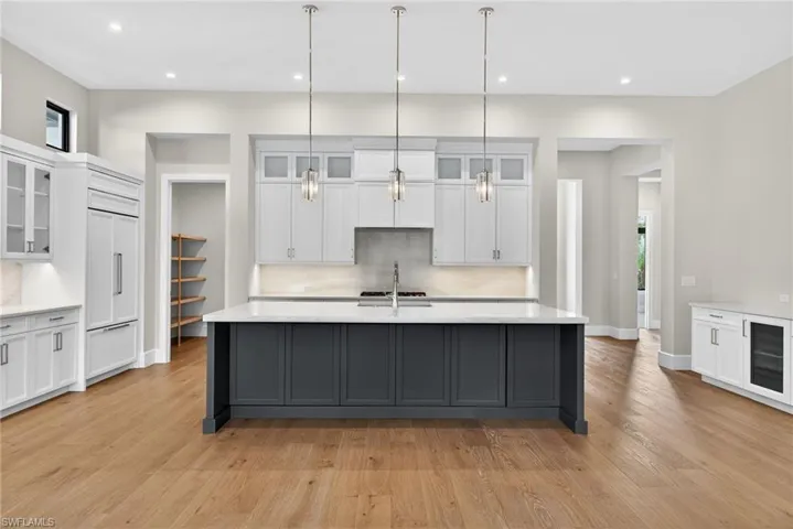Two tone kitchen featuring glass fronted cabinets, two tone cabinetry, pendant lighting, decorative backsplash, and a large island