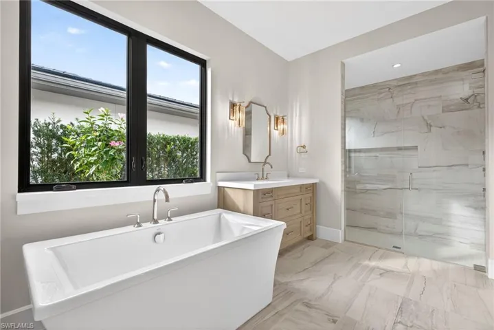 Full bath with light marble finish floors, vanity, a marble finish shower, and a freestanding tub