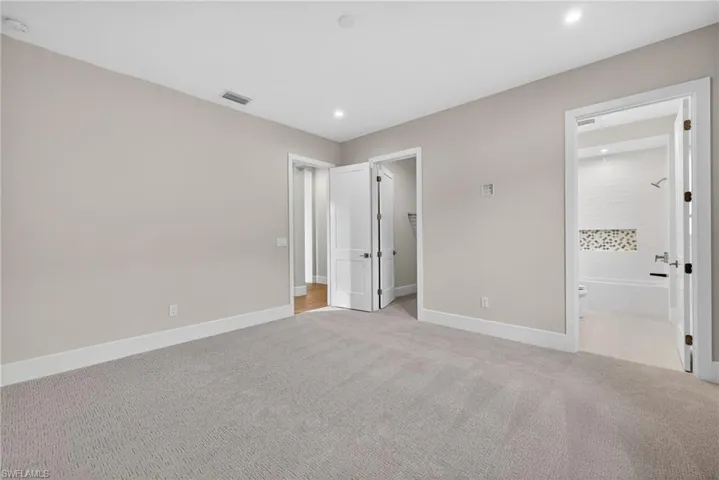 Bedroom 1 with a spacious closet, light colored carpet, recessed lighting, and ensuite bath