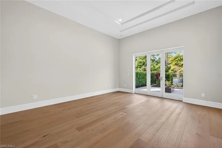 This primary bedroom featuring light wood flooring and a high tray ceiling, French doors leading to private outdoor patio space with fire pit