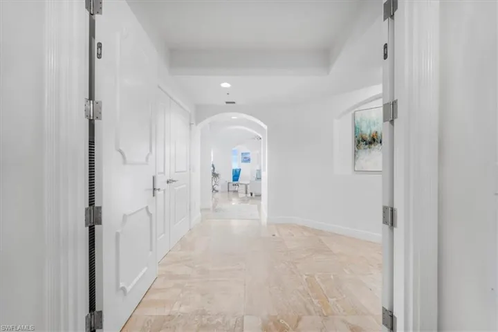 Corridor with arched walkways, light marble finish flooring, and recessed lighting