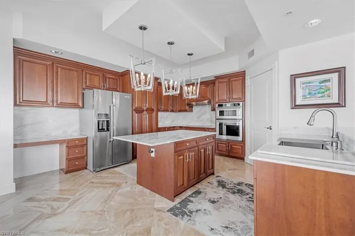 Kitchen featuring brown cabinetry, appliances with stainless steel finishes, light stone countertops, and a kitchen island