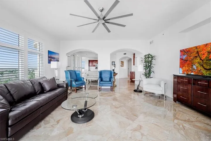 Living room with arched walkways, light marble finish flooring, and a ceiling fan