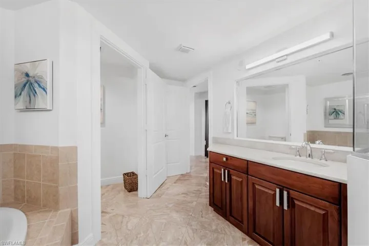 Full bath featuring vanity, tiled tub, and light marble finish flooring