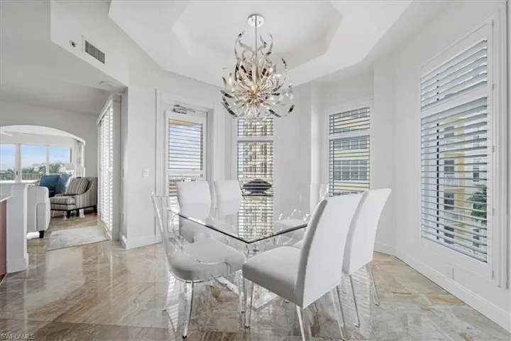 Dining area featuring a chandelier, light marble finish flooring, a tray ceiling, and arched walkways
