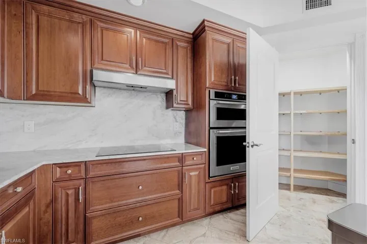 Kitchen featuring brown cabinetry, under cabinet range hood, stainless steel double oven, and light stone counters