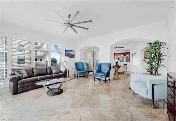 Living area with arched walkways, light marble finish floors, and ceiling fan