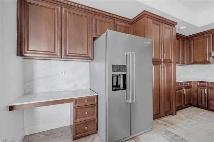 Kitchen with high quality fridge, built in study area, light marble finish flooring, and light stone countertops