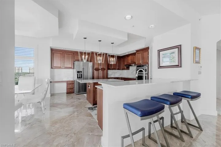 Kitchen with a breakfast bar area, a tray ceiling, hanging light fixtures, appliances with stainless steel finishes, and light stone counters