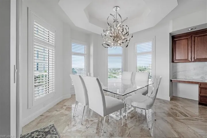 Dining area with built in study area, a chandelier, light marble finish floors, and a tray ceiling
