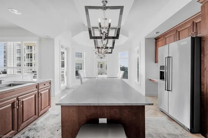 Kitchen featuring high end refrigerator, light stone countertops, a center island, and brown cabinets