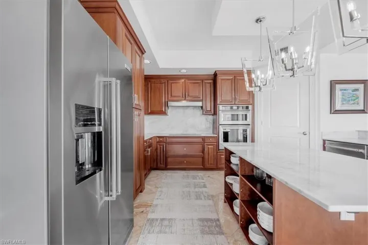 Kitchen featuring open shelves, stainless steel appliances, pendant lighting, brown cabinetry, and light stone countertops