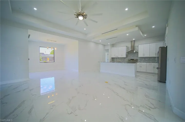 Unfurnished living room with a tray ceiling, light marble finish floors, recessed lighting, and a ceiling fan