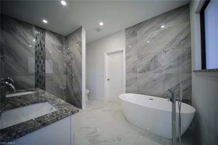 Bathroom with tile walls, a soaking tub, light marble finish floors, a marble finish shower, and stone wall