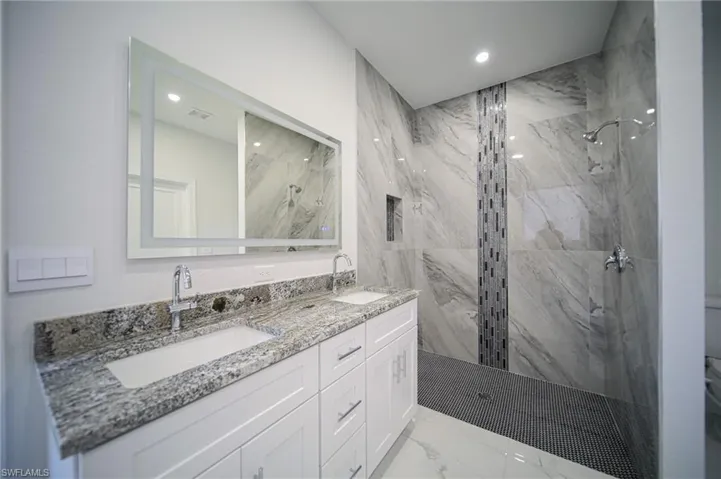 Bathroom with light marble finish floors, double vanity, a marble finish shower, and recessed lighting