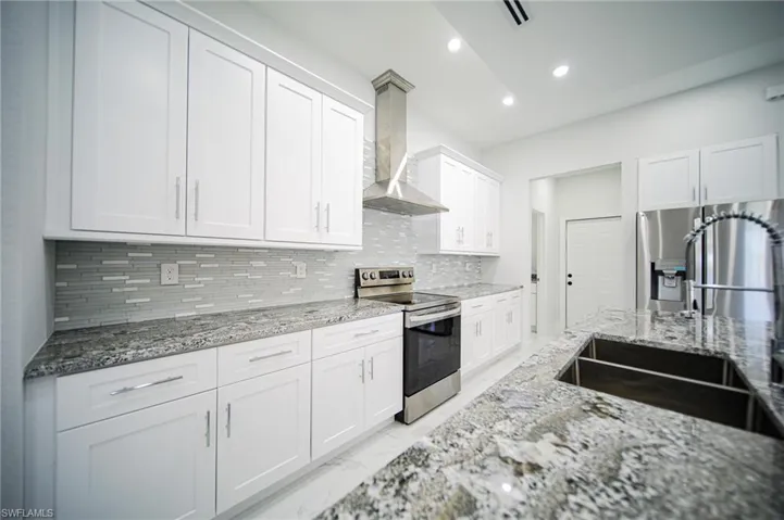 Kitchen featuring stainless steel appliances, light marble finish flooring, light stone counters, wall chimney exhaust hood, and white cabinets