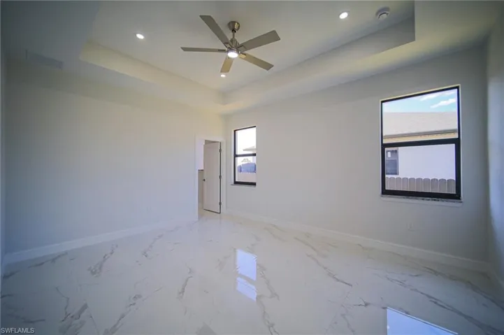 Spare room featuring light marble finish floors, a raised ceiling, recessed lighting, and ceiling fan