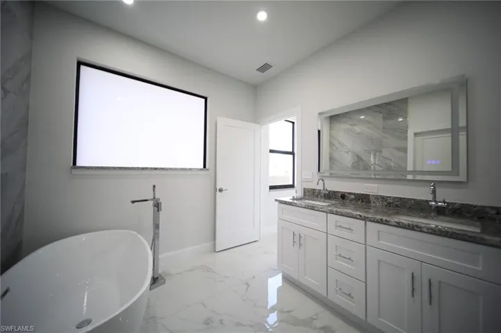 Full bath featuring a freestanding bath, double vanity, light marble finish flooring, and recessed lighting
