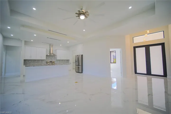 Unfurnished living room with a raised ceiling, light marble finish flooring, recessed lighting, and a ceiling fan