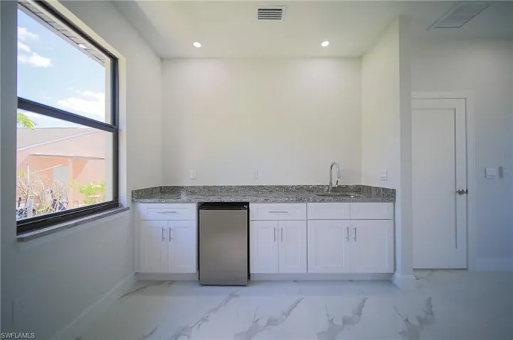 Kitchen featuring light stone countertops, white cabinetry, stainless steel refrigerator, light marble finish floors, and recessed lighting