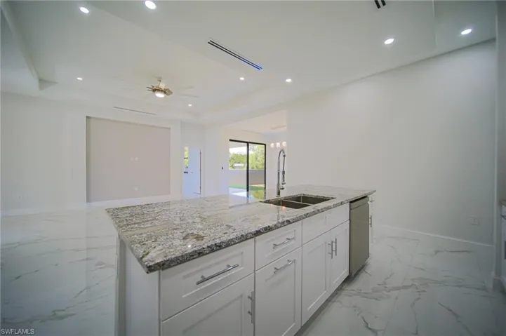 Kitchen featuring light stone counters, white cabinetry, an island with sink, recessed lighting, and a tray ceiling