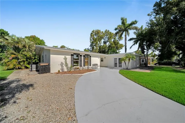 White stucco exterior with black window shutters and a curved paved driveway