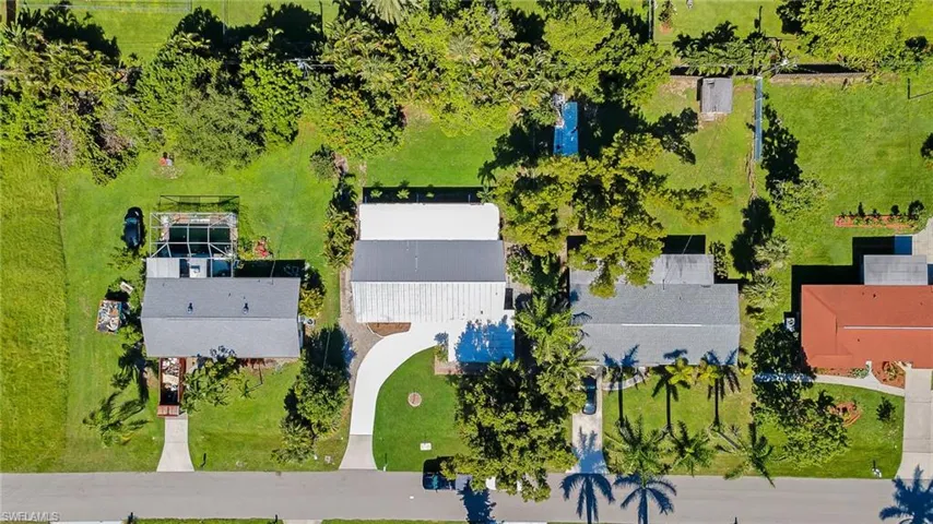 Aerial overview showcasing a property with a screen-enclosed pool, expansive green spaces, mature trees, and a paved driveway