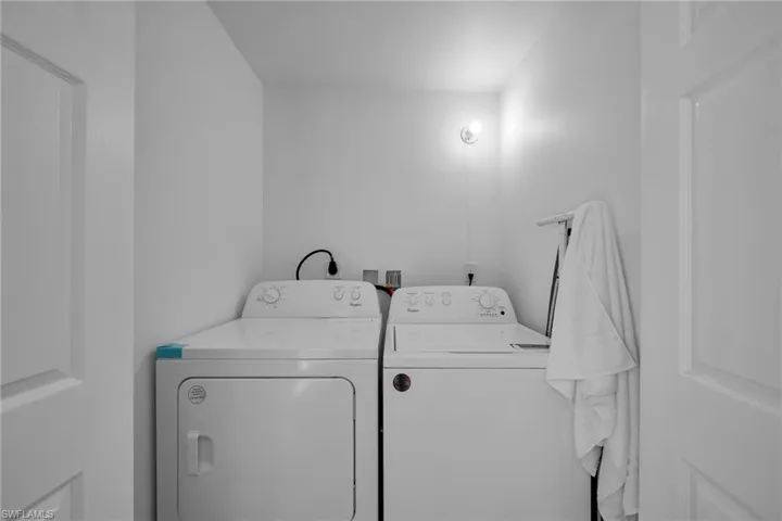 Dedicated laundry area featuring white appliances, a wall-mounted light fixture, and neutral painted walls