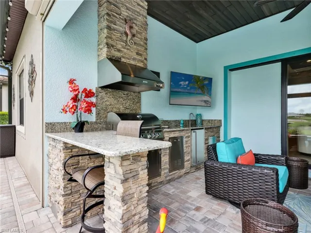Covered Lanai with Wood Plank Ceiling & Ceiling Fan, Outdoor Stacked Stone Kitchen with Granite Top, Gas Grill, Stainless Steel Beverage Fridge, and Sink