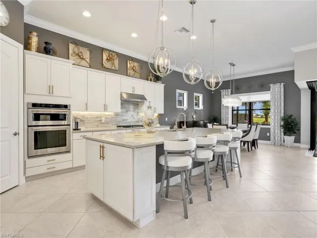 Gourmet Kitchen with KitchenAid Stainless Steel Double Wall Oven with Top Speed Oven, Gas Cooktop, Hood, & Dishwasher, Tile Backsplash, Large Island with Storage, Single Basin Stainless Steel Sink, RO Water Filter, Pendant Lighting, Walk-In Pantry, & Dining Area with Battery Powered Motorized Shade, Custom Curtains & Golf Course View.