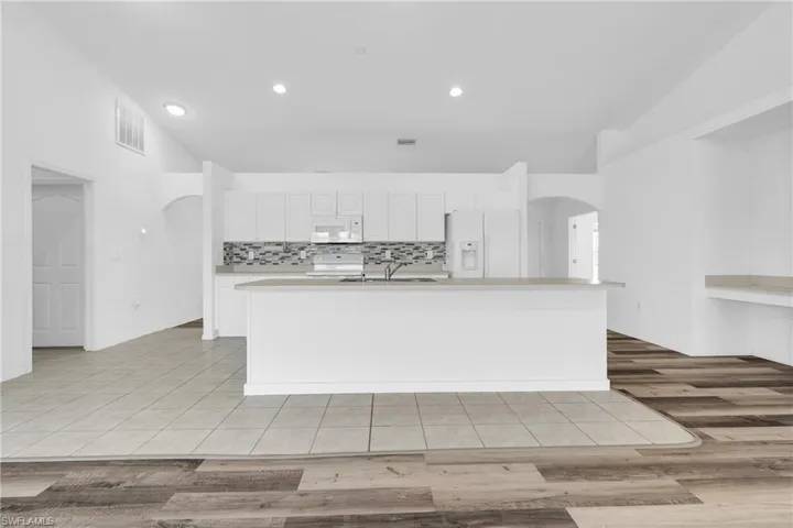Kitchen featuring visible vents, arched walkways, a sink, light countertops, and white appliances