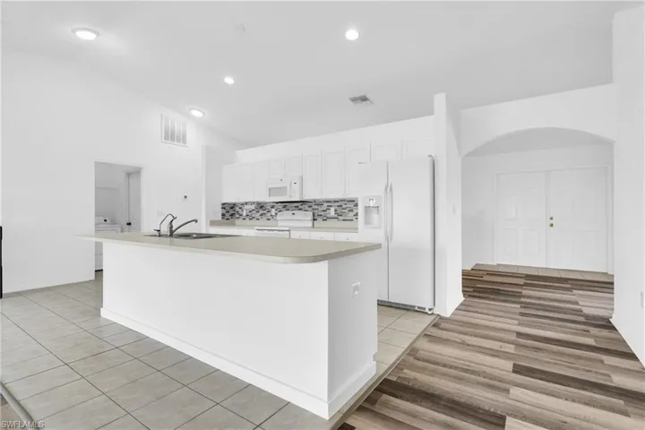Kitchen featuring white appliances, visible vents, a center island with sink, and light countertops