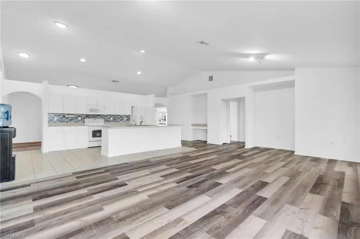 Unfurnished living room featuring visible vents, recessed lighting, arched walkways, light wood finished floors, and vaulted ceiling