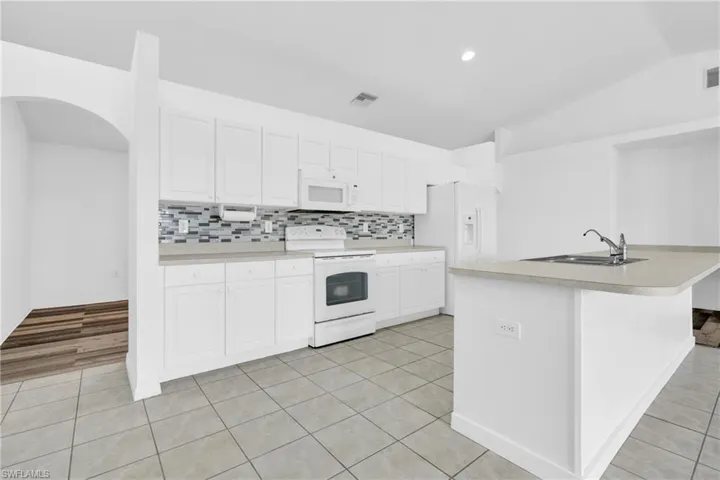 Kitchen featuring a sink, visible vents, white appliances, white cabinetry, and vaulted ceiling
