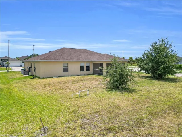 Back of house with a lawn, central air condition unit, stucco siding, and a garage