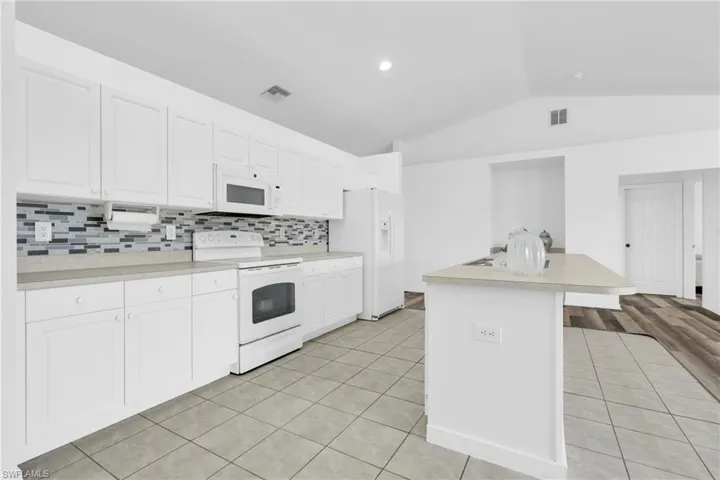 Kitchen featuring white appliances, visible vents, light tile patterned floors, and lofted ceiling