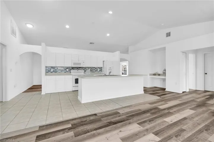 Kitchen featuring white appliances, arched walkways, visible vents, and lofted ceiling