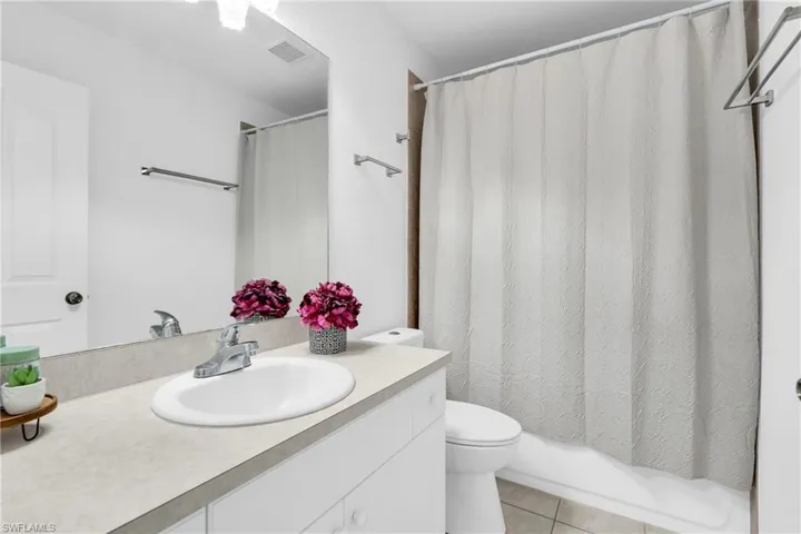 Bathroom with shower / bath combination with curtain, visible vents, tile patterned flooring, vanity, and toilet