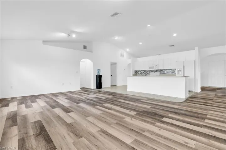 Unfurnished living room featuring arched walkways, visible vents, light wood-style flooring, and recessed lighting